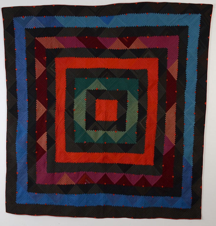 This richly colored quilt is a Barnraising Log Cabin on square instead of the more usual way of setting it on point. It is made of solid color wools with printed cotton for the backing. Tiny red centers are like jewels scattered throughout the quilt