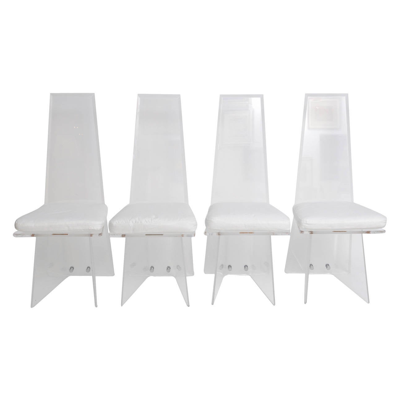 Four sculptural lucite chairs with tapered high backs and angular bases. Chromed screw covers connect the bases to the backs. Cushions newly covered in bright white cotton fabric easily reupholstered in the fabric of your choice and attached to the