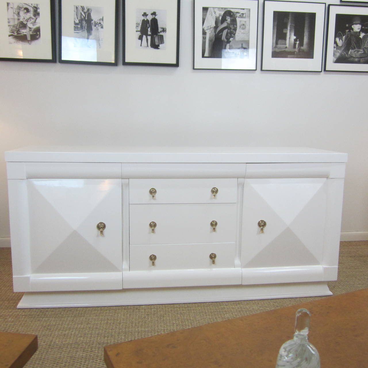 A beautifully finished 1950s credenza with raised diamond front doors flanking three center drawers, all with original recently polished brass hardware.  
Perfectly finished inside and out in durable high gloss white lacquer, this credenza has