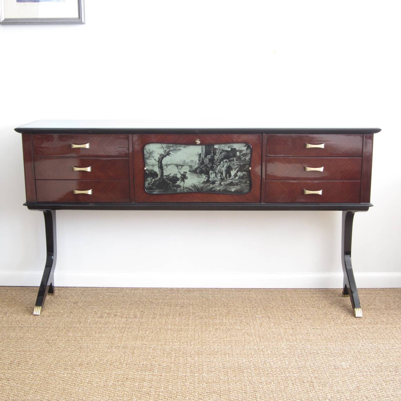Tall Italian console in mahogany with reverse painted glass center panel. Drop down center door has original skeleton key and the inside is mirrored with small individual pieces. The long legs are split at the bottom and the fronts are capped. The