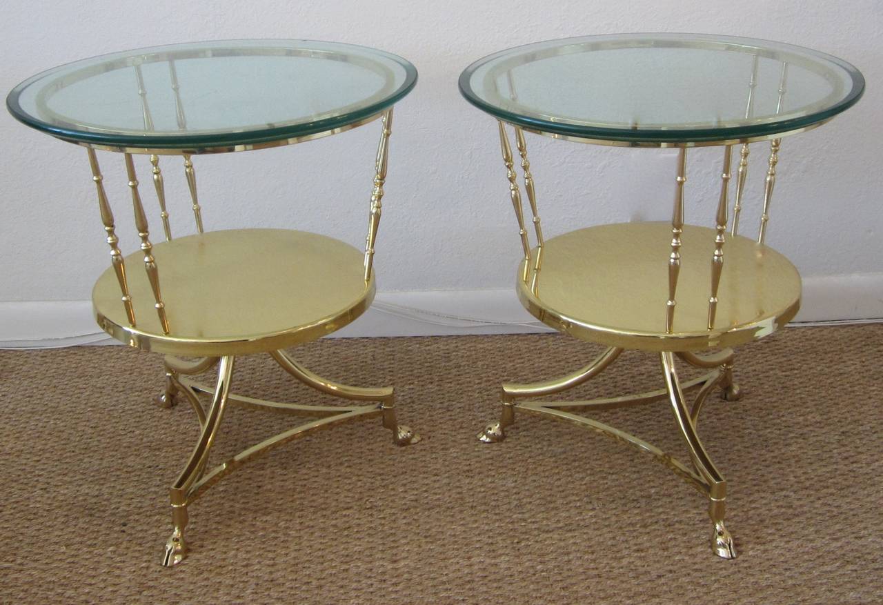 Pair of brass two-tier tripod side tables with clawed feet and glass tops.