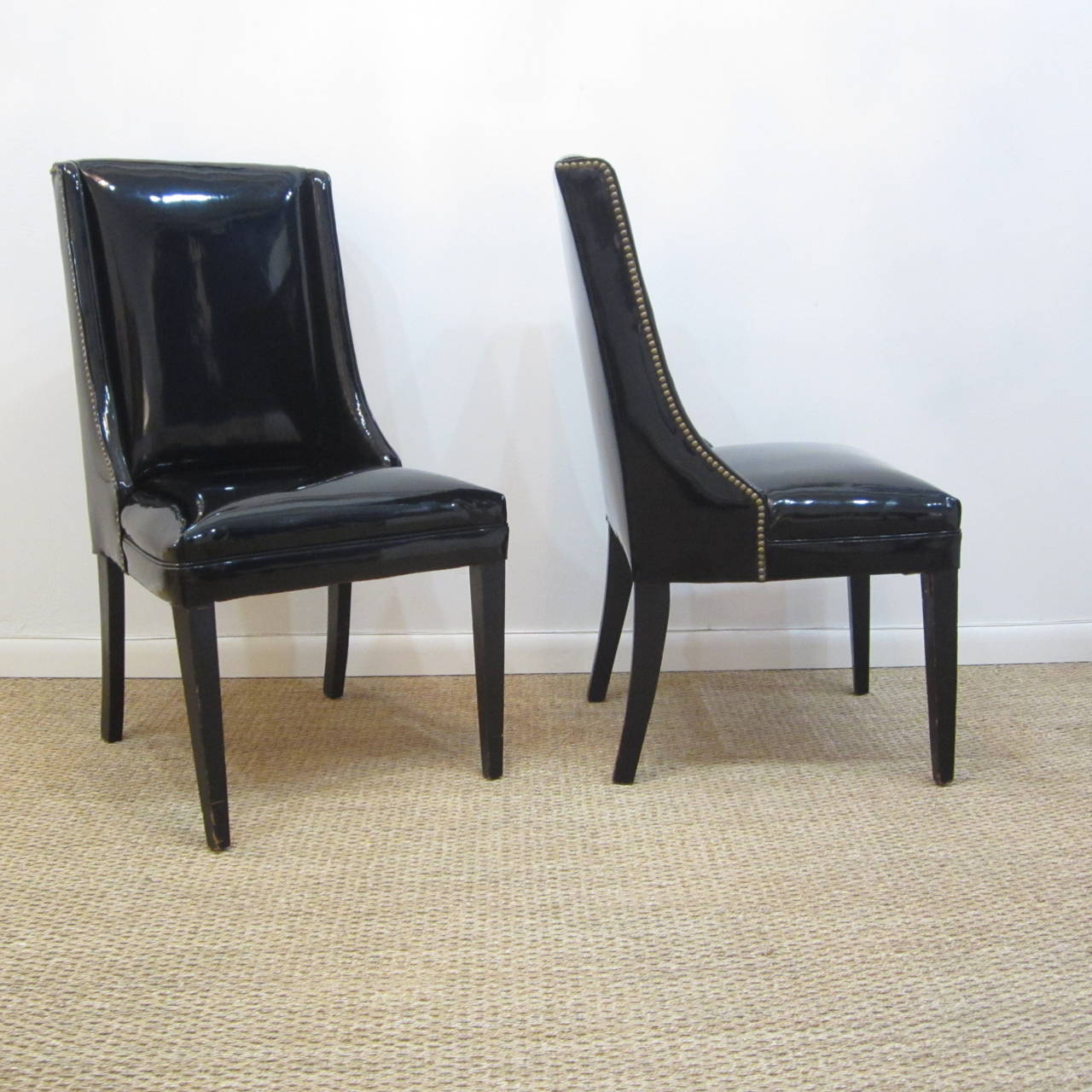 Pair of midcentury side chairs in patent leather with brass studs. The legs are black painted wood with natural ware. These chairs are solid and sturdy and in original condition with tiny imperfections adding  to their beauty.