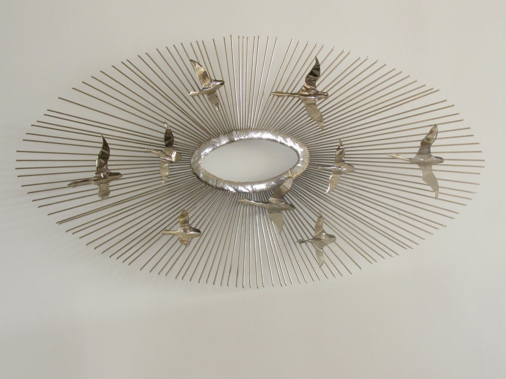 Metal oval shaped wall sculpture with thin metal birds attached in flight.
