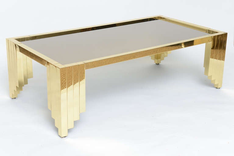 As seen in Architectural Digest September 2014
Stunning polished brass cocktail table with stepped up skyscraper designed  legs. Recessed bronze mirrored top exquisitely compliments the high polished brass which is clear coated for lasting