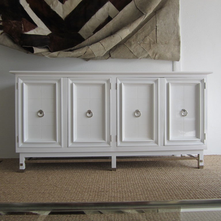 Four doored white lacquered cabinet with nickel cross bars, feet caps, square pegs, and hinges. Each door has nickeled neoclassical ring pulls and reveals two shelves with one being adjustable. Great elegant storage.