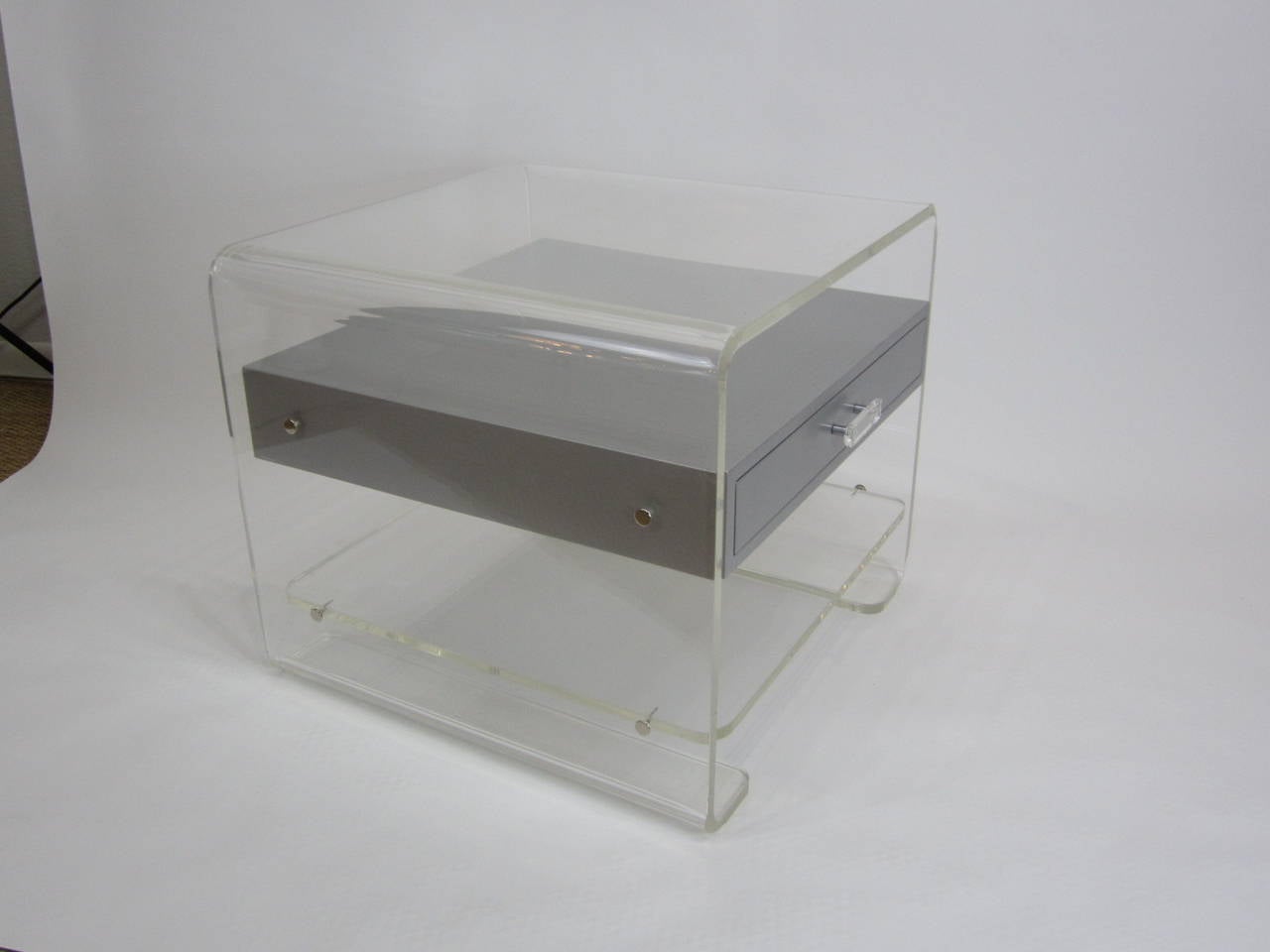 Fantastic rounded edge Lucite side table with suspended silver lacquered wood drawer on gliders. The soft sloped sides are mimicked at the bottom where the Lucite curves back inward creating the base. The edges are beveled and the screws holding the