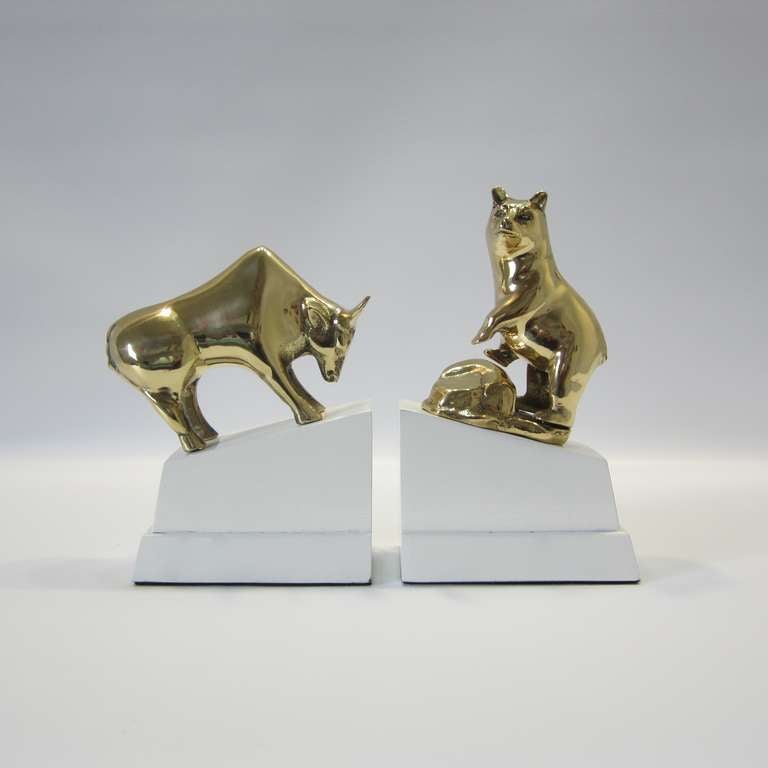 Polished brass bull and bear bookends mounted on high gloss white lacquered wood bases. Dynamic sharp contrast between the brass and the white! Makes a great gift.