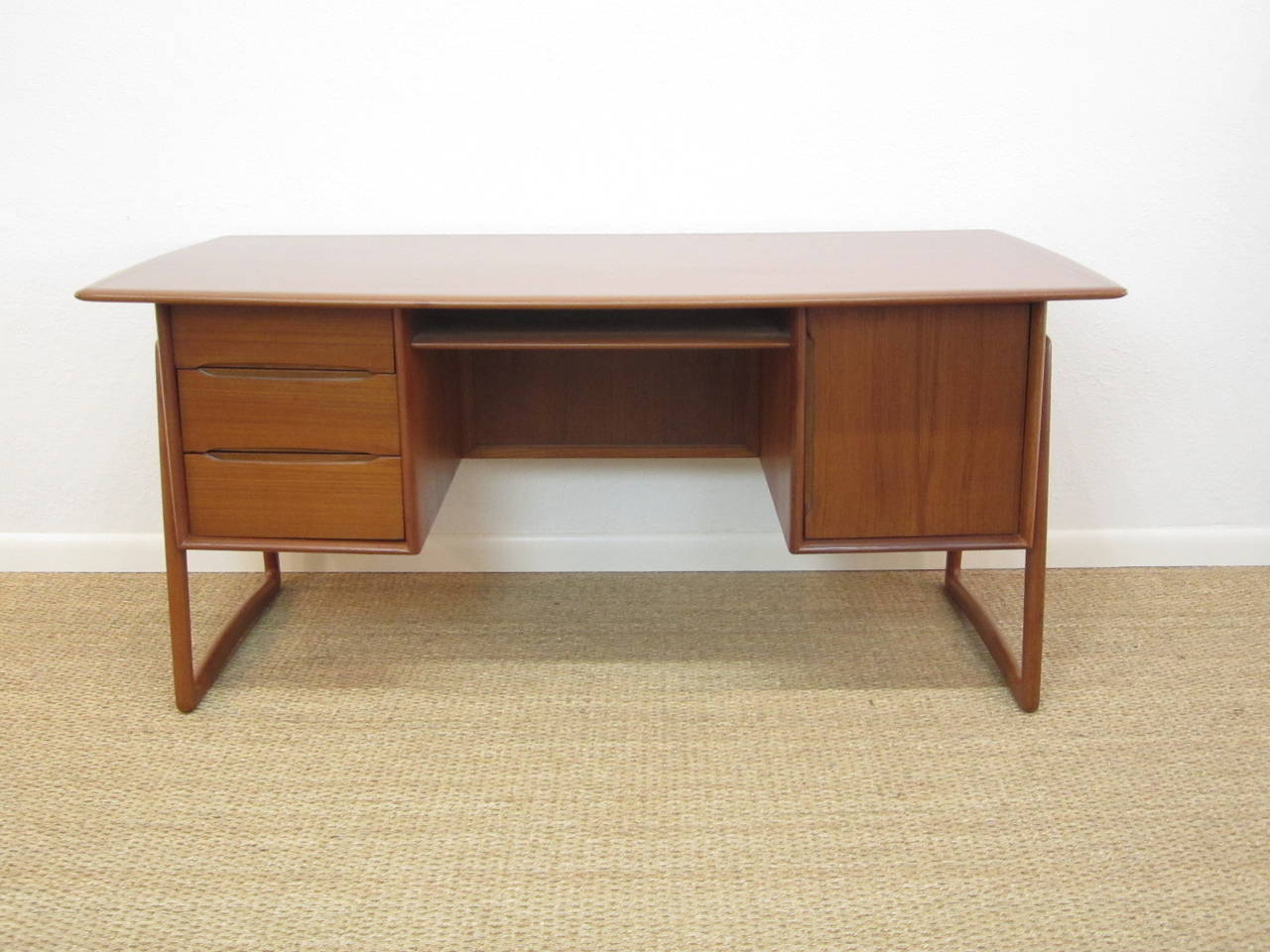 Finely finished Danish teak desk with raffia insert facing forward. Finished all the way around so can float as an executive desk. Center paper slot, right hand door, and left hand drawers--finished inside and out.