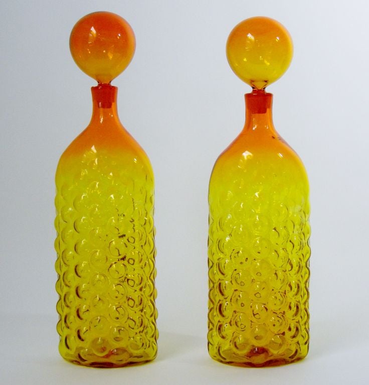 Gorgeous and rare pair of decanters in amberina; the classical color design fading from yellow to orange to red. Original balloon stoppers are also rare to find in this mint condition--no cloudiness or chips. These decanters are 22 inches tall and