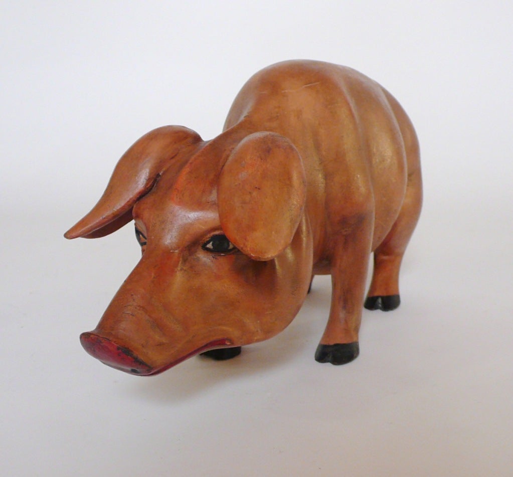 A carved wooden sculpture depicting a pig , hand painted, with an iron tail.