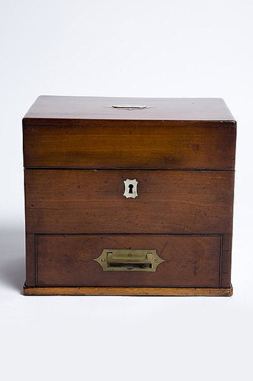 Mahogany and brass box, with a lower drawer in the front. By opening the top, secured with singes on the back, the upper part reveals an internal cover in blue silk with a group of glass bottles ( some with labels) placed in separate compartments.