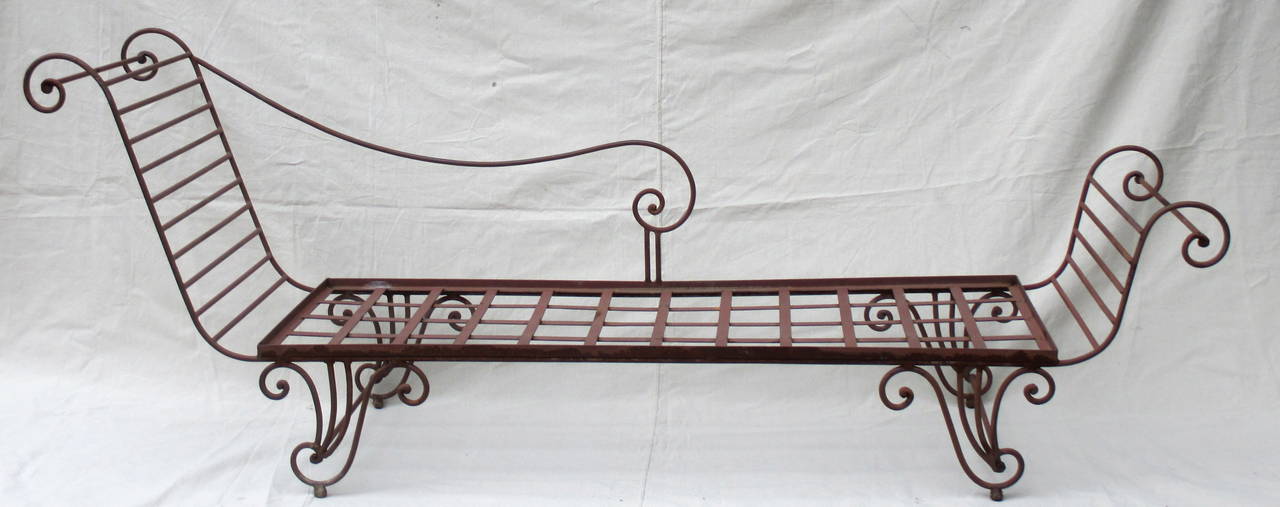 Wonderful scrolling wrought iron chaises longues in original red paint with weathered surface. Some rust which adds to the patina of these heavy iron lounges. Originally made for patio use, but would be great indoors. Hard to find an opposing pair