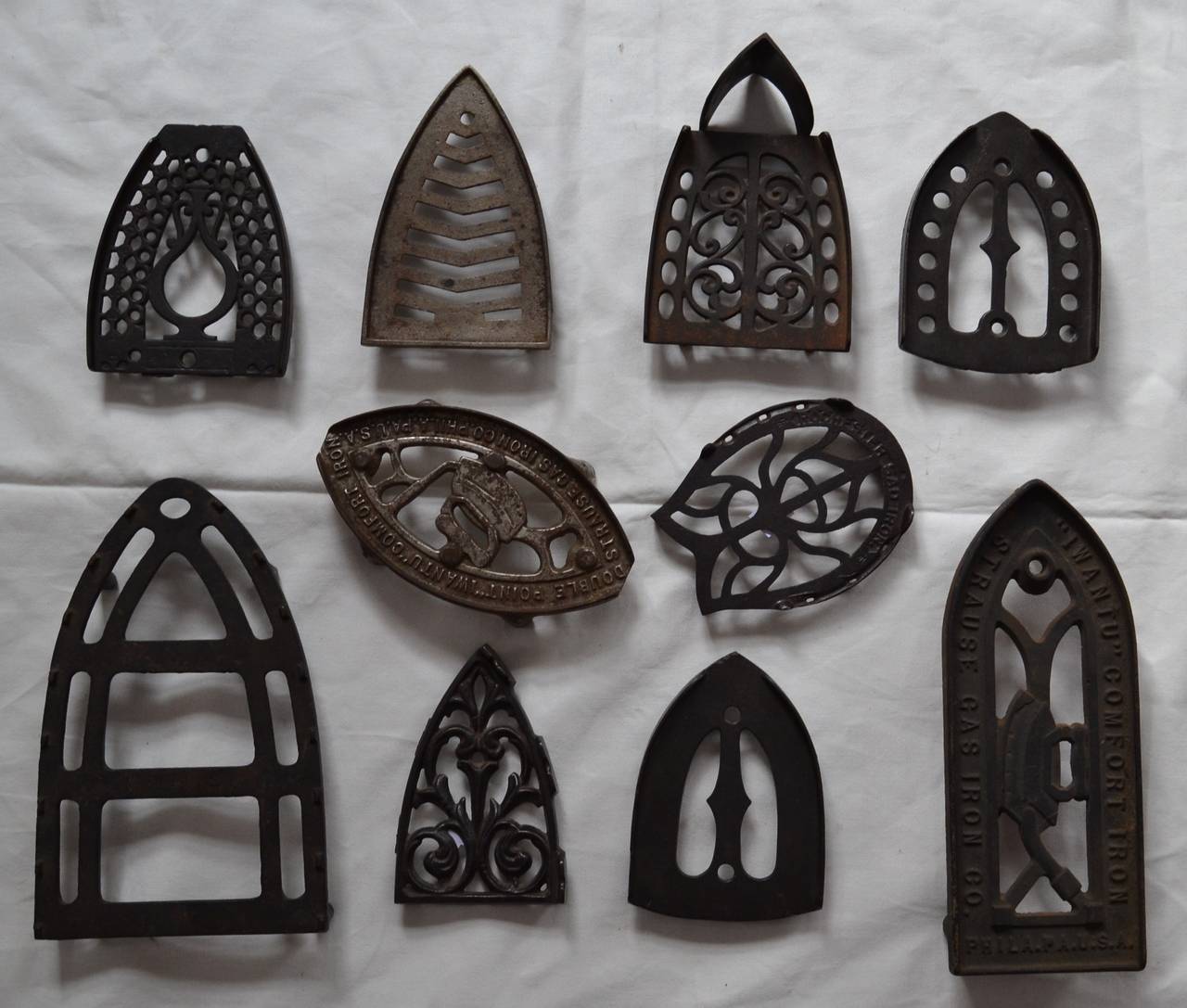 A variety of designs and sizes of sad iron trivets, nice graphic collection showcasing Victorian industrial design. Variety of sizes between 11 inches tall and 7 inches wide.