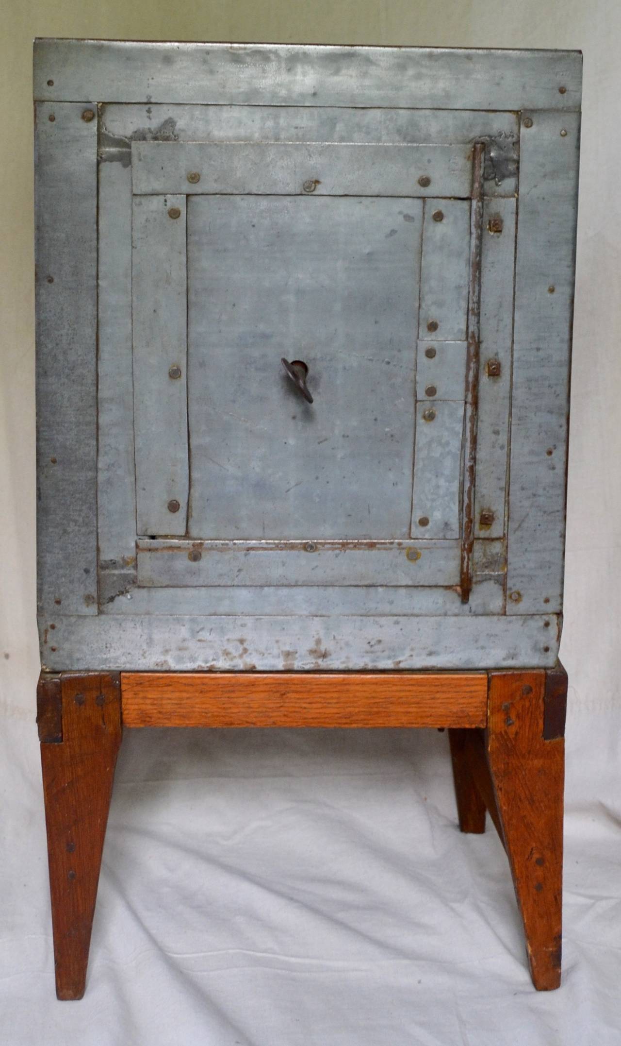 Assembled patchwork zinc covers the wooden interior of this folk made safe. Hand made locking mechanism and key. the safe sits on pine legs. an elegant folky gesture, great height for use as a side table. a popular rendering of an object that is