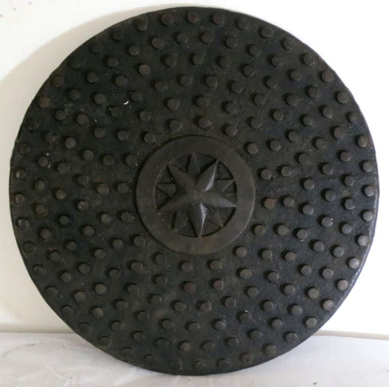 Cast iron industrial cover with a graphic pattern of raised dots and a central star.