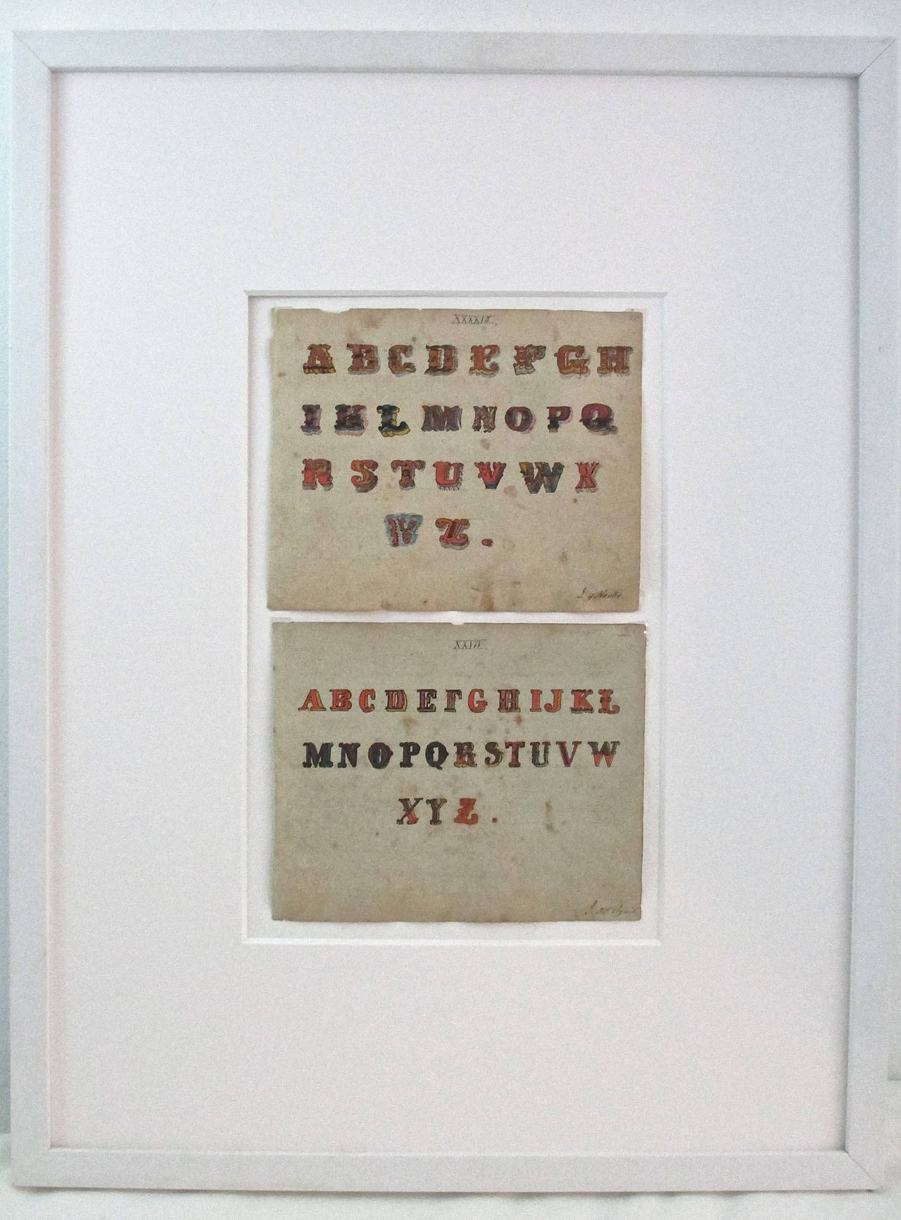 Two mid-19th C  Watercolor alphabet samplers using interesting fonts.  The two pages, by an anonymous artist, are framed together in a contemporary white frame.  Each is drawn on a a 6.5