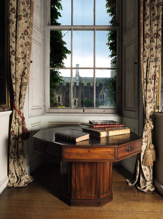 A George II mahogany rent table.<br />
<br />
The revolving octagonal top with a rare cloth inset decorated to simulate needlework with a central vignette of a garden and a viaduct, surrounded by anthemion and floral borders, the frieze fitted