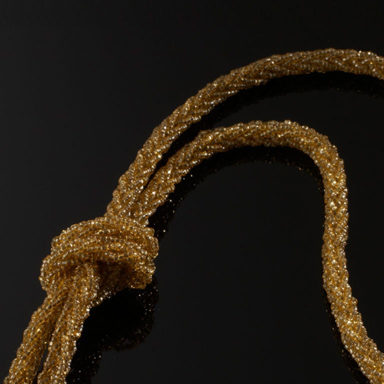 A gold necklace made up of glass beads which can be adjusted to fit as a choker or any length you require
Looped tassle end