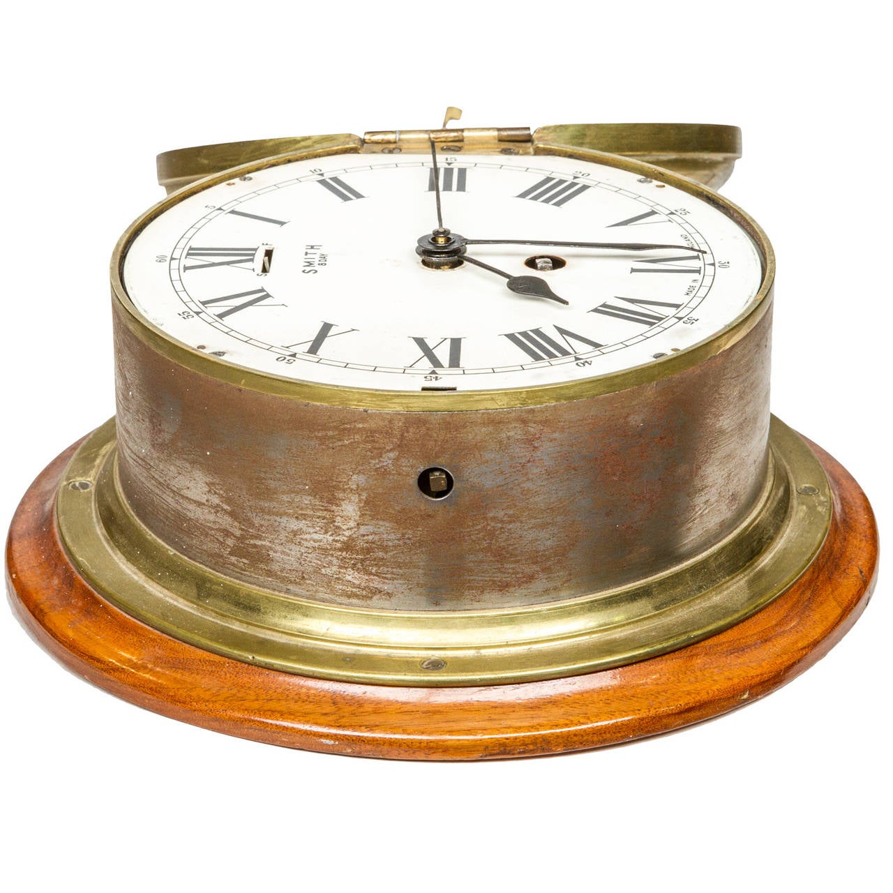 The clock is housed in a heavy brass and steel case. The case is attached to a finished mahogany platform. The white enamel clock face has roman numerals with the minutes in denominations of five. The clock was made in England and is in good working