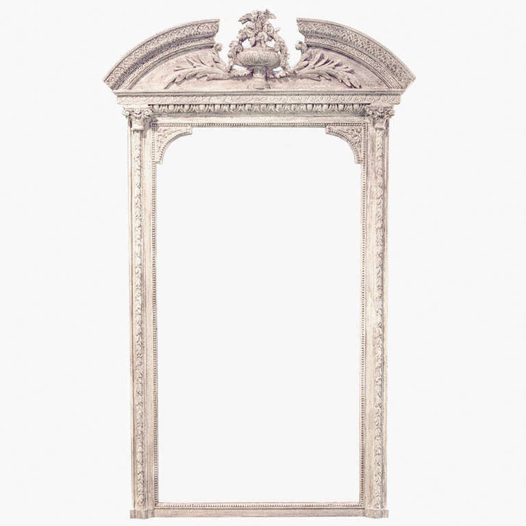 A 19th century French painted wall mirror. The top is designed with a broken arch pediment and centered is a stunning carved floral basket. All of the wood and gesso carving really highlights the mirror. Capitals on the right and left.