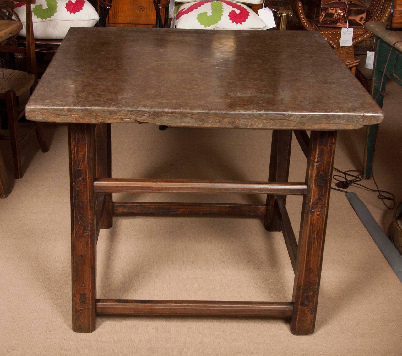 A striking newly polished stone top surmounting an antique Asian elmwood table base.