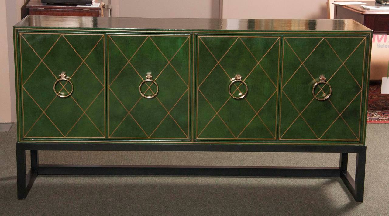 A Tommi Parzinger for Charak Modern credenza having green leather finish tooled and gilded in a lozenge pattern and two cabinets each with two double doors with circular brass hardware. The interior of each cabinet fitted with a single drawer over a