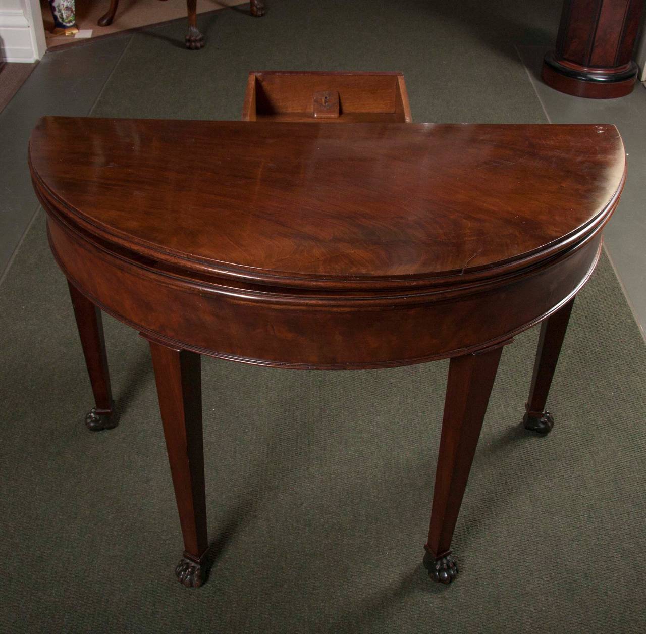 A Louis Philippe style mahogany, D-shaped games table with a folding top and a green-leather lined interior surface. The five tapered legs are terminated in carved paw feet.