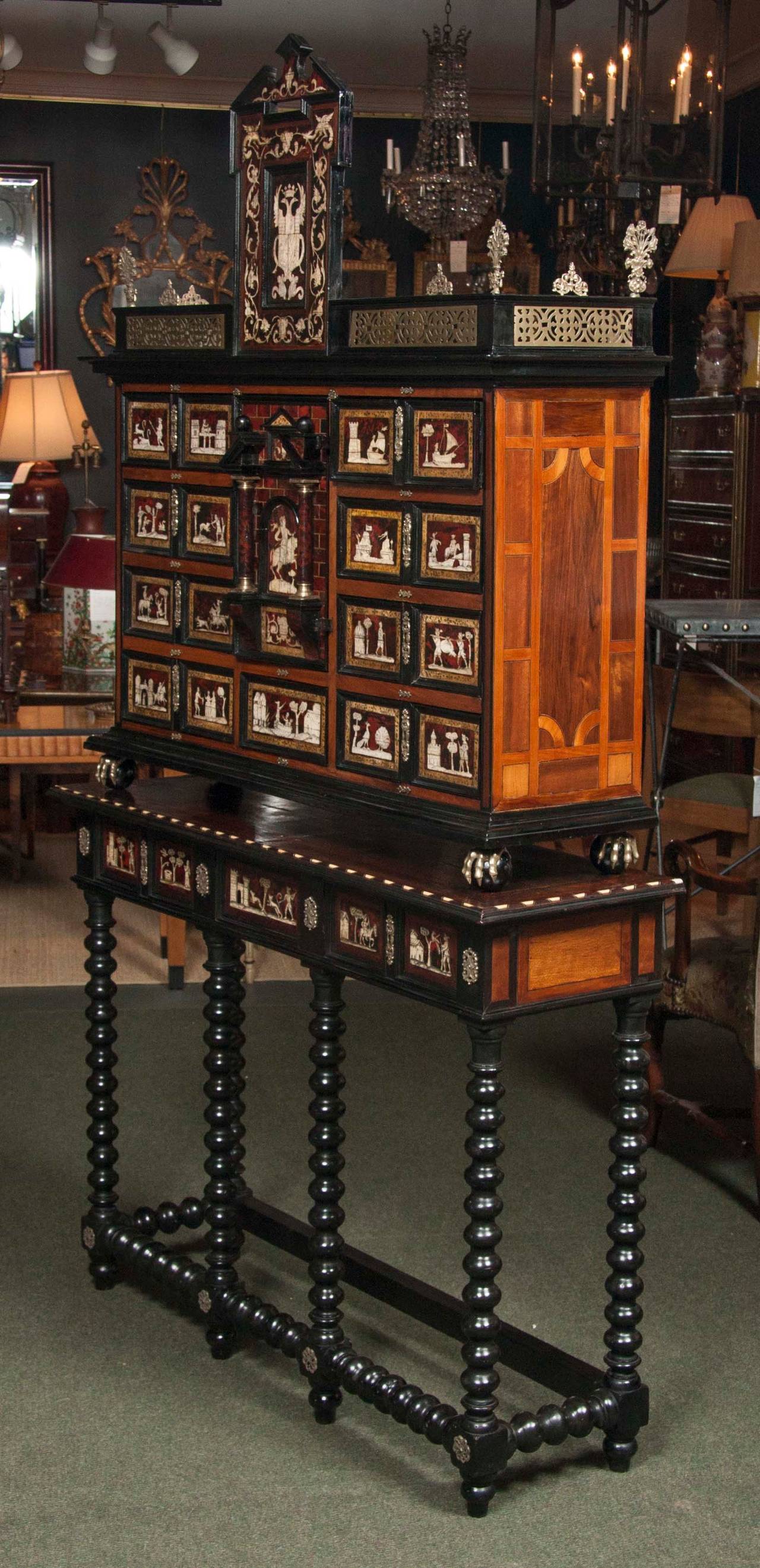 A Spanish tortoiseshell and bone inlaid, ebonized walnut marquetry cabinet on stand.  The upper section with a pediment with a double headed eagle surmounted by a crown and family crest.  A center door, bordered by columns, reveals four interior