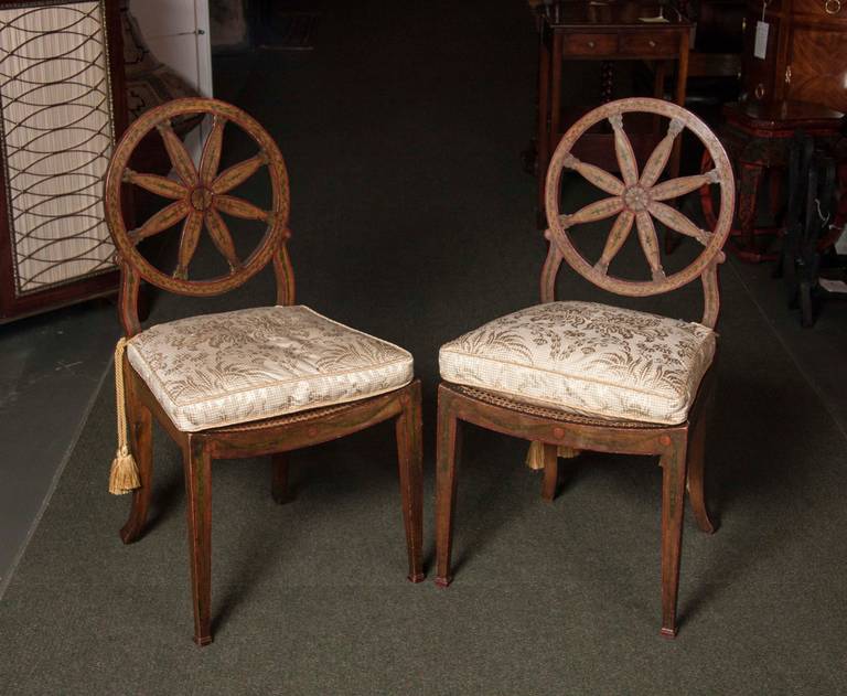 A pair of wheel-back painted and caned side chairs and cushions in the George III style.