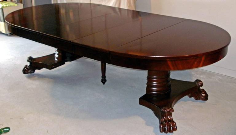 An early 19th century American Empire period mahogany dining table on a divided neoclassic column (housing a turned support leg) on a shaped mahogany veneered platform supported by impressive hand-carved lion's paw feet, includes three solid