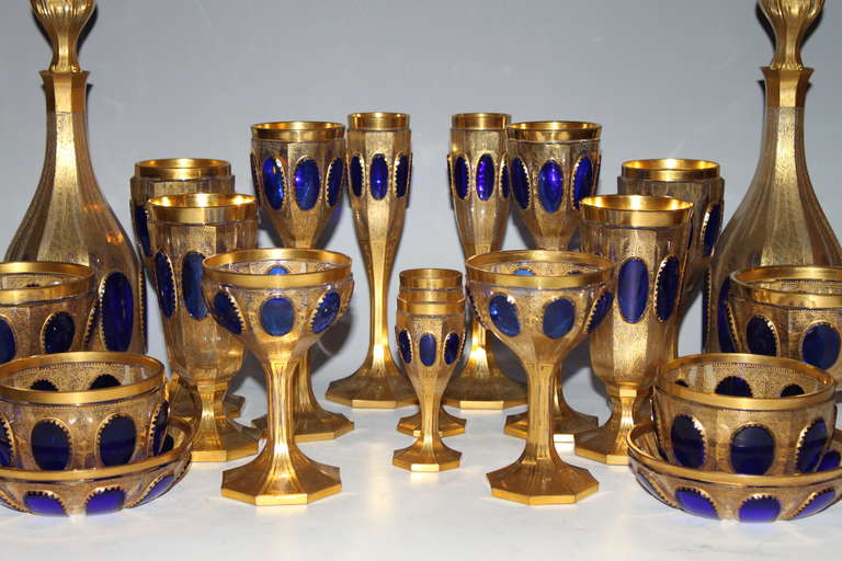 An extensive and quite rare sapphire cabochon and clear double overlay Moser glass stemware and dessert service. The royal blue cabochons complement the hand diamond cut glass further adorned with 24 karat gold highlights all over. This set is an