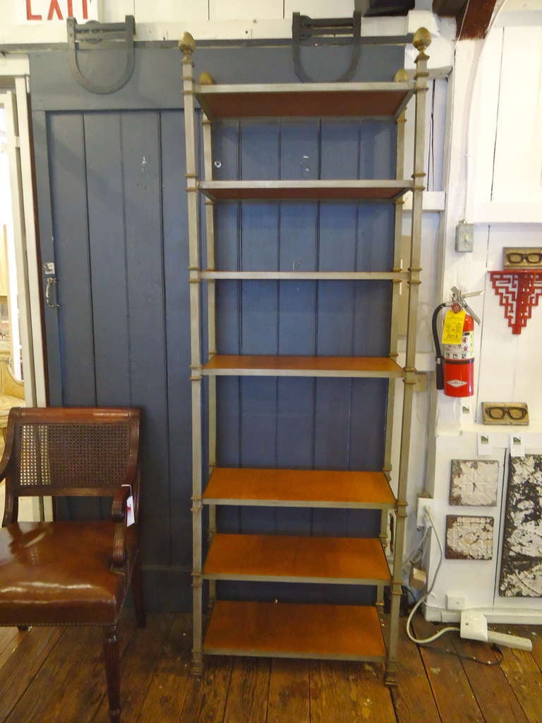 Tall, narrow, classically styled etagere with 7 shelves. Came from the estate of Cole Porter. Surface of shelves are light brown leather; structure is painted iron in a matt nickel.  Decorative brass pineapple finials.
Shelves pop out for easy