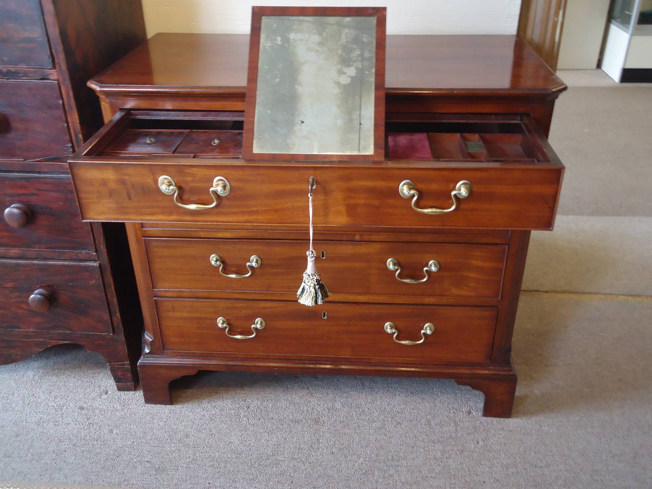 George III Mahogany Bachelor’s Chest, circa 1780, the overhanging canted top above four graduated cock beaded drawers retaining their original brasses, the top drawer fitted with dusting slide opening to reveal a series of cubby holes with lids and