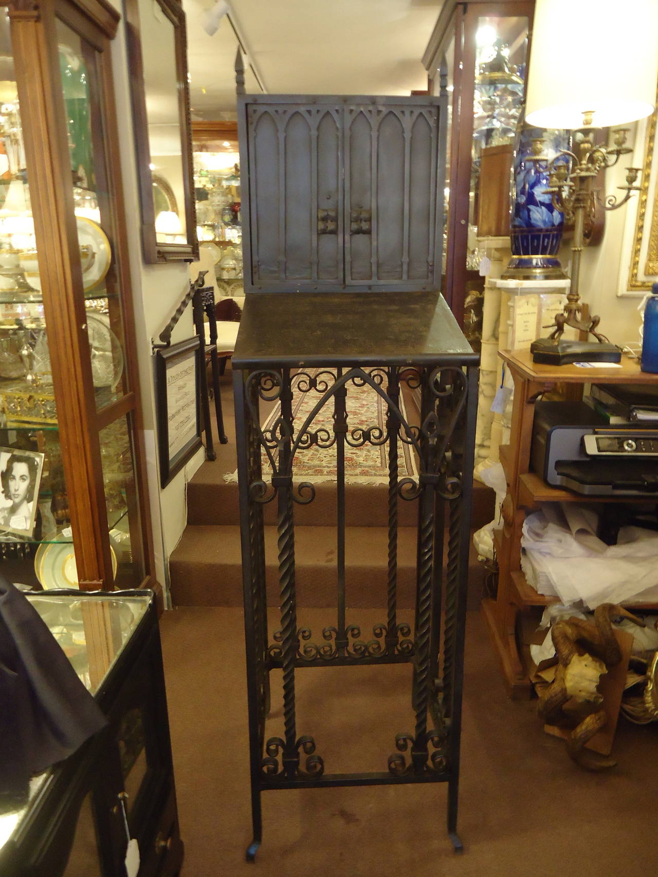 Black wrought iron sculptural stand having two doors with shallow interior space for storage of papers or keys and a writing surface. Curlicue decorative base and religious letters on the back. Most likely came from a church.
Would make a great