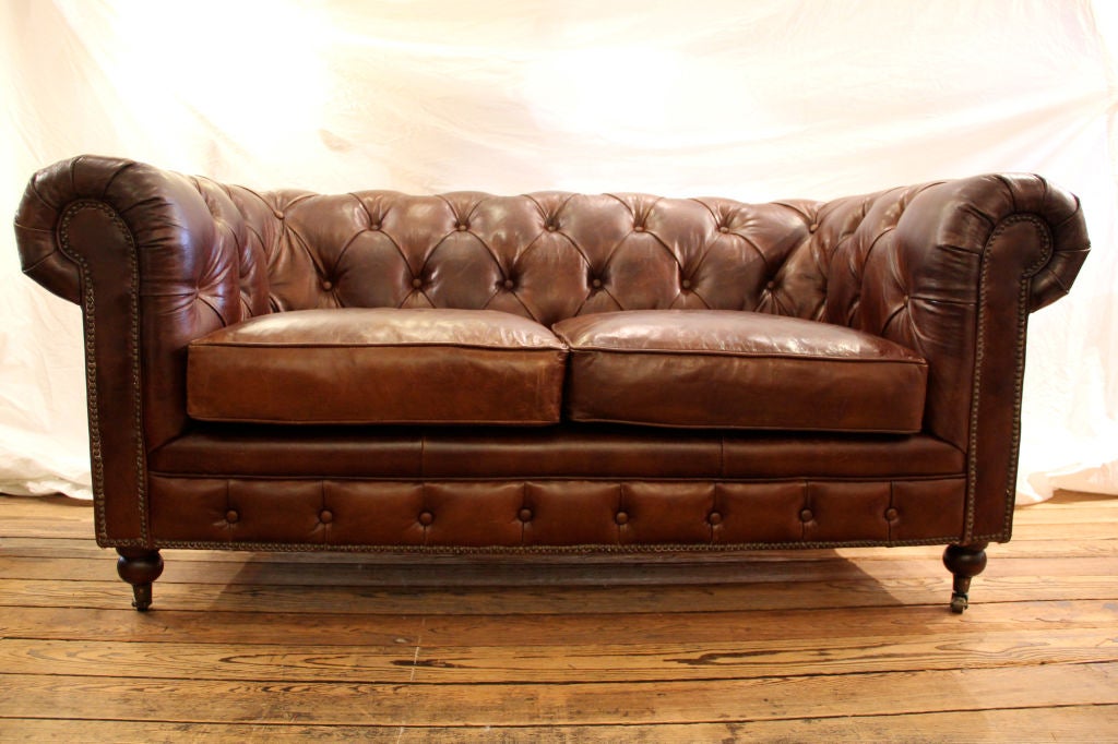 Imported, leather tufted brown sumptuous small sofa with nailhead detailing, legs are fitted with wheels, Looks old but is new as far as we know