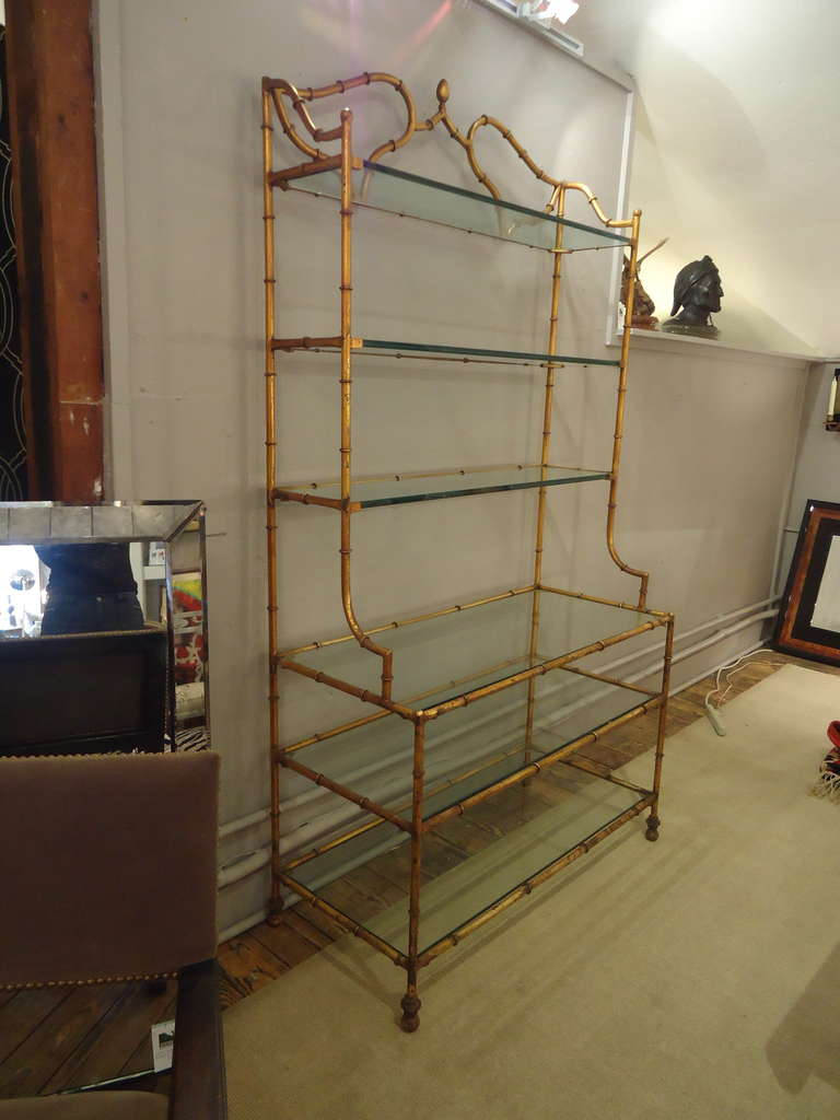 Unique form with a step back style. Gilded metal with  6 custom thick cut glass shelves.  Has a nice worn rustic gilt patina.
