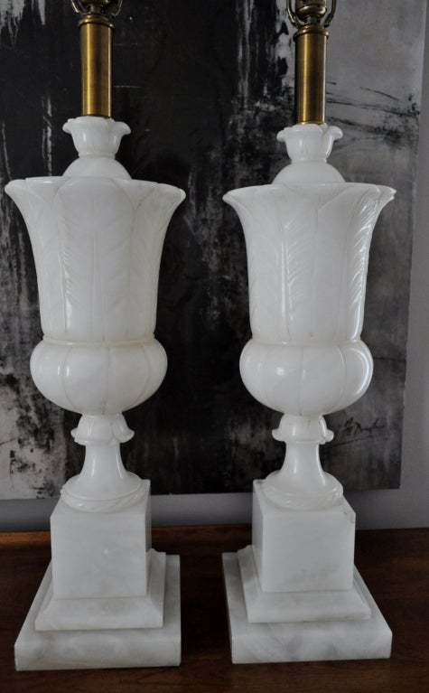 Grand pair of alabaster urn lamps in classical style by Paul Hanson.  Beautiful carved detailing.  Original harps and alabaster finials.  Original Paul Hanson label on one socket.  
 7 inch square base.  Urn 8 inch diameter.