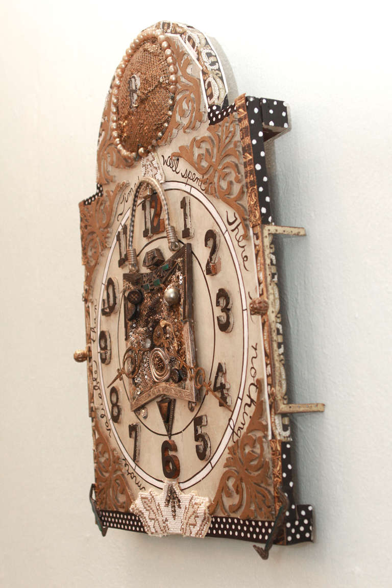 Elements include a silver frame from a vintage pocketbook, bits and pieces of silver and gold mesh, buttons, charms, etc. The old clock face is adorned with cigar labels in black and gold that say 
