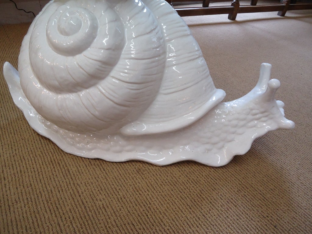 Charming white ceramic snail sculpture that is a base for a diminutive cocktail table with an irregular shaped oval glass top