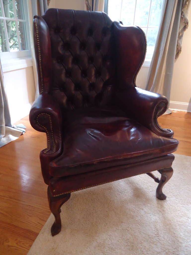 English, early 20th century oxblood leather wing chairs; loose seat cushions and tufted backs flanked by roll arms accented with brass nailheads.  Short cabriole legs with slipper feet.  Seat depth 24