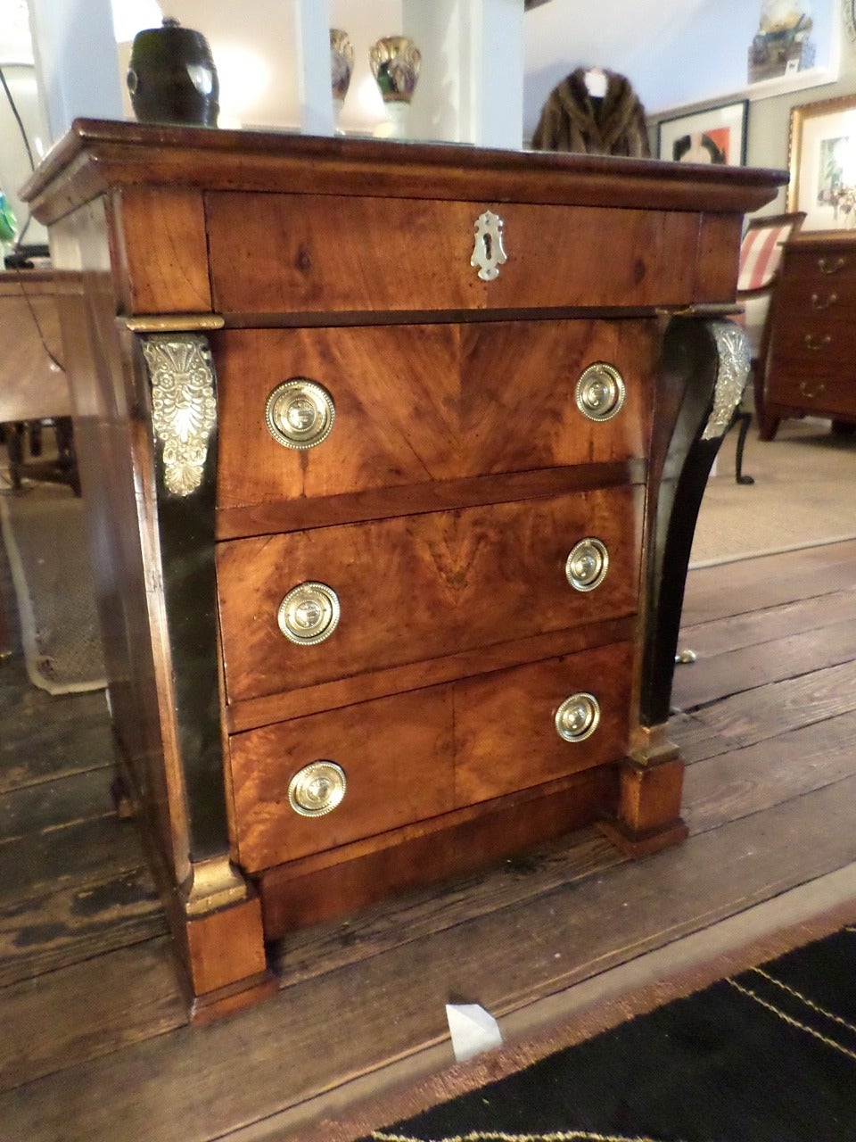 Diminutive French Empire mahogany chest of drawers, circa 1820, with a superb mellow patina, the overhanging top above four drawers flanked by curved ebonized pilasters with gilt accents on the capitals, all resting on a plinth base. Rare small