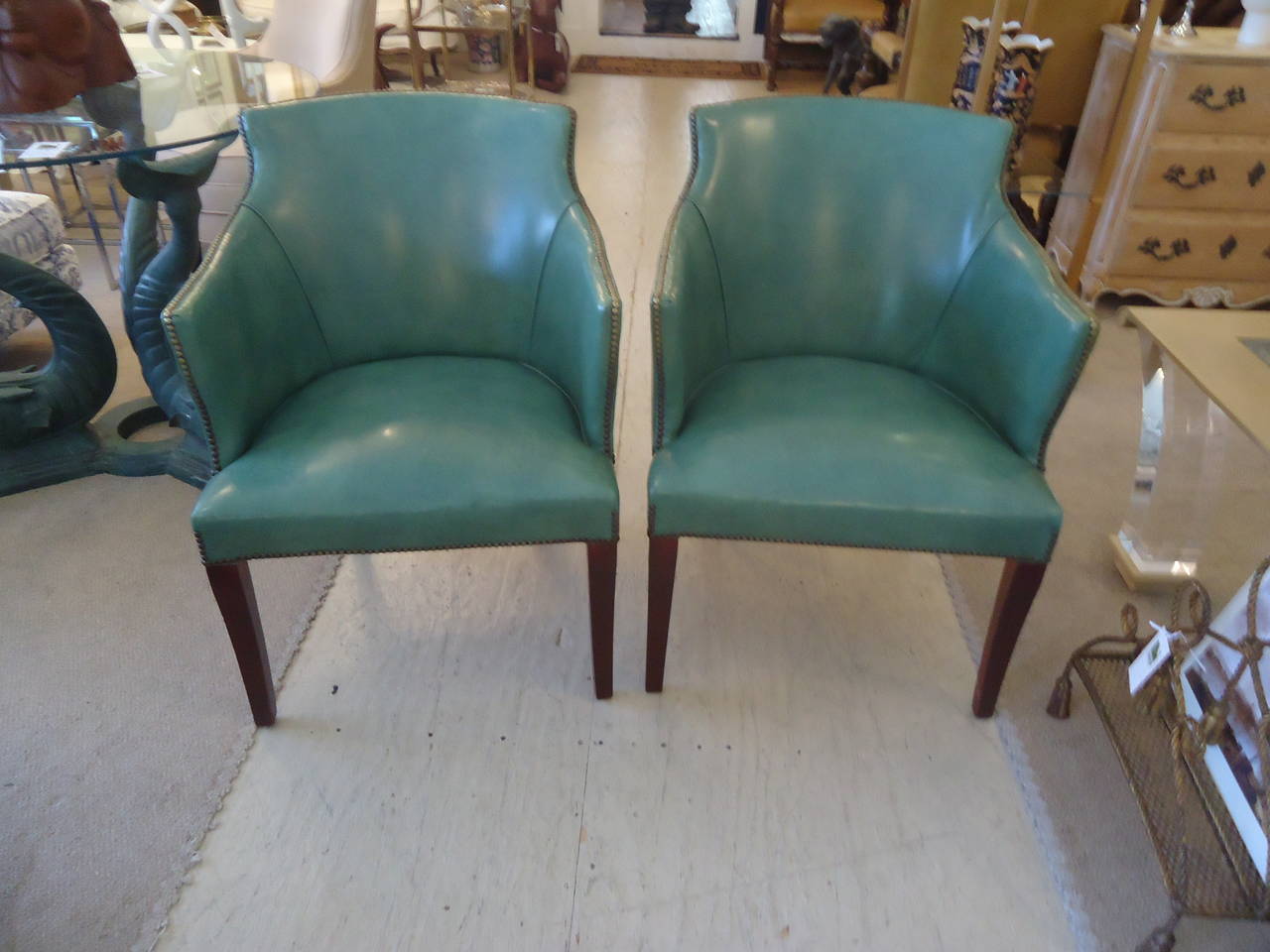 Beautiful tailored lines on this pair of vintage barrel back tub chairs covered in soothing sea foam bluish green leather, finished with bronze colored nailheads, sitting on tapered mahogany legs. Firm, very comfortable chairs.
Seat depth 19
