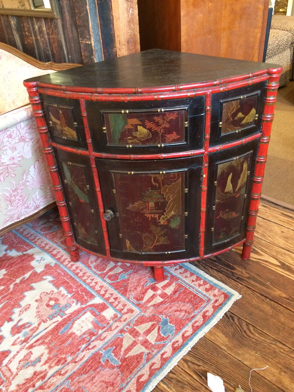 Elegant pair of corner cabinets, hand-painted chinoiserie style in black, red, green and gold. Faux bamboo periphery is tomato red and gold. Inside interior has one shelf.