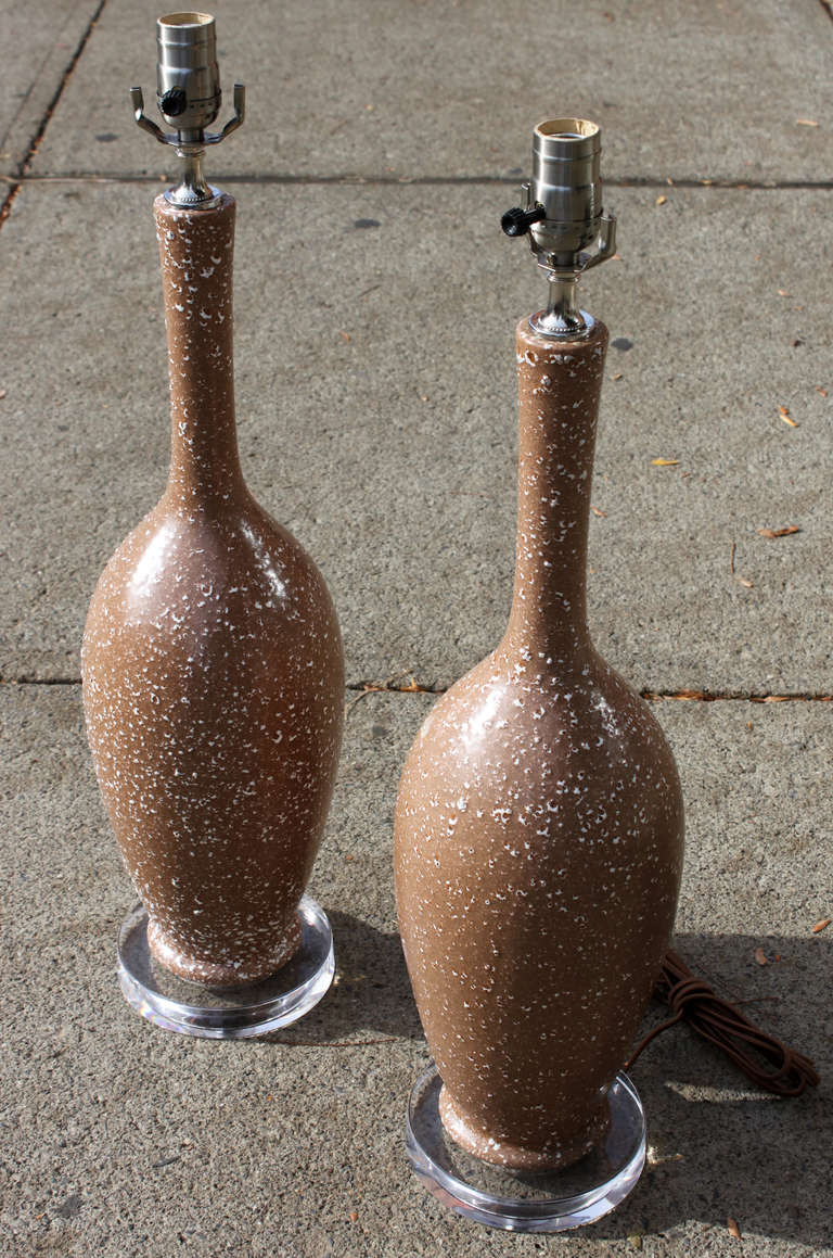 Nice pair of bottle form mid century table lamps. A richly creamy mocha with a white pebble glaze adorns this pair of lamps which sit atop a clear acrylic disc base. Newly rewired.