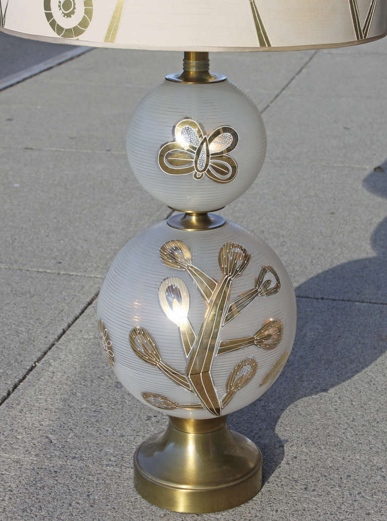 Large double glass globe and brass fitted table lamps. Each globe is frosted in a horizontal ring pattern with applied gold floral and butterfly motif topped with a white drip glaze. The pair of lamps retain their original 20