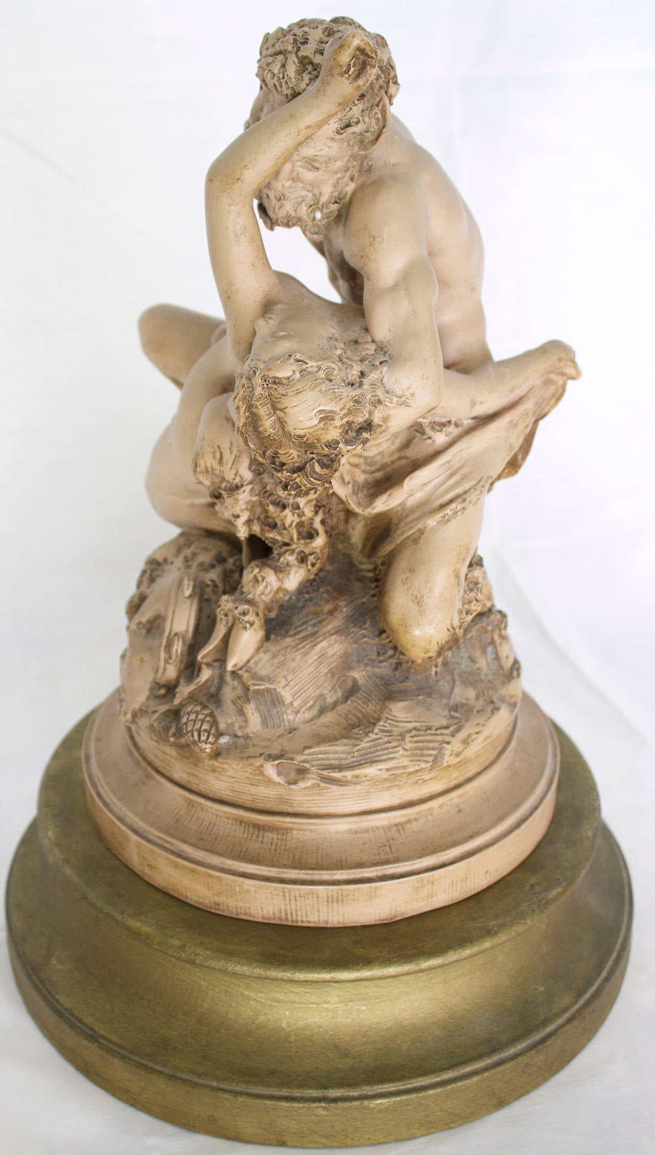 Terracotta group representing a Satyr detaining a resisting Bacchante. It rest on a cylindrical base surmounted by a rock on which there is tambourine, thyrsus and wine Amphora. Signed Carrier- Belleuse. The sculpture is on a gilded wood