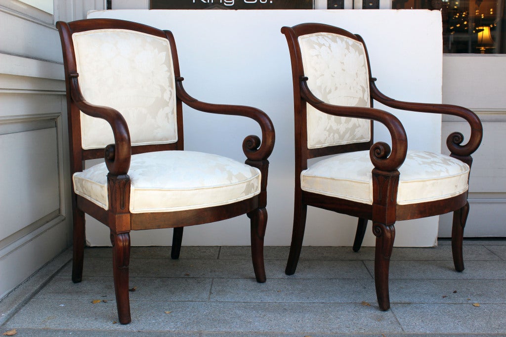 Elegant pair of mahogany Restauration period armchairs, France, circa 1820. Typical French Restauration armchairs with a slightly arched back over graceful scrolled armrests with carved decoration. The bowed seat and its apron are raised by carved