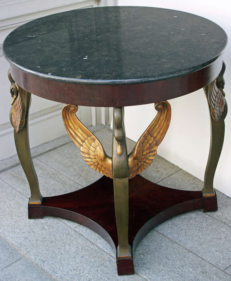 This center table also called Gueridon is in dark mahogany veneer and patinated wood with four baluster feet having wooden swan spreading their gilded wings to hold the cincture.
The feet are linked by a four concave faces stretcher tablette.