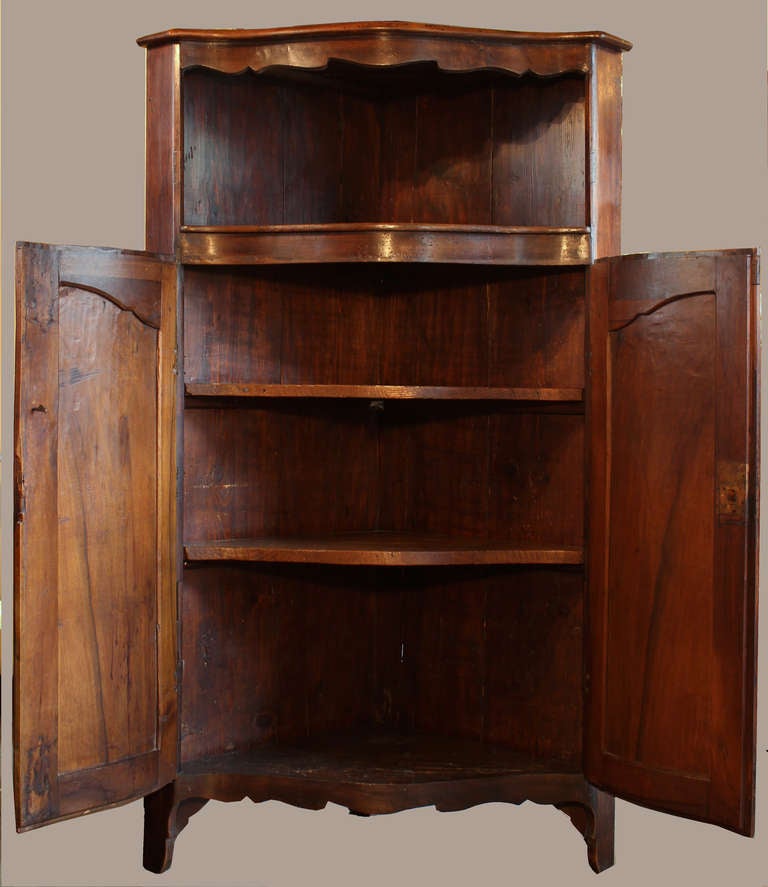 Magnificent patina and design for this walnut Corner Cabinet which open's by a pair of hand carved front doors in a bow shape ,hiding 3 shelves inside.The 