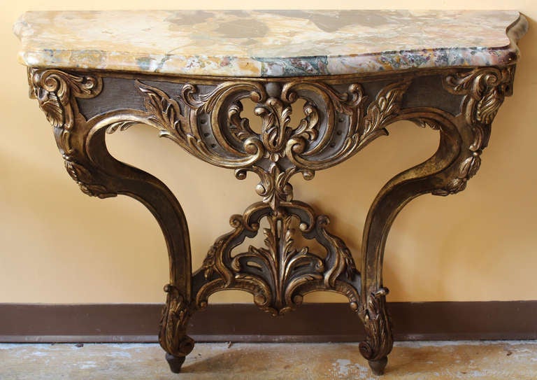 Beautifully carved, gilded and painted wood console table with a gorgeous marble top.
It shows curved lined and sinuous movement with great wood carving of stylized doré foliages, rinceaux and coquilles. Chantourne and moulure Breccia marble top in